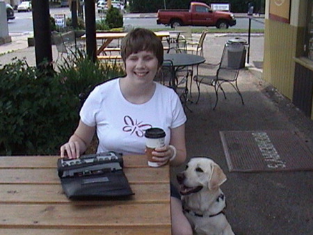 Nickie sitting outside a coffee shop at a table holding a cup of coffee.