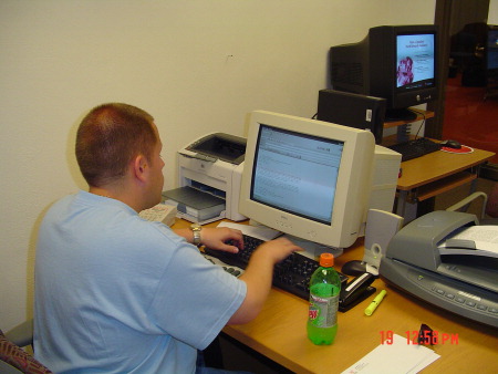 Photo of T. J. sitting at his desk surrounded by equipment.