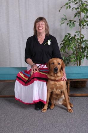 A woman sits on a bench next to a dog guide.