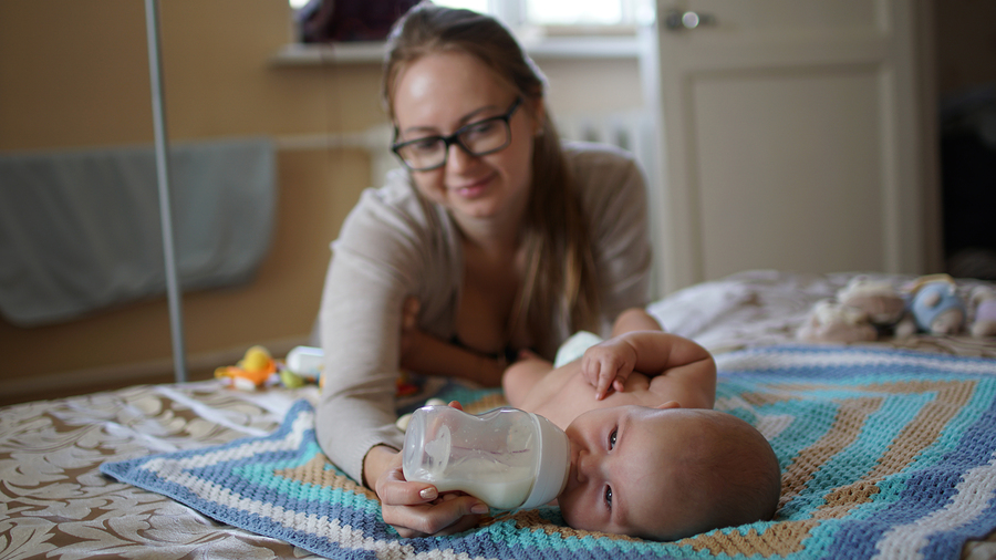 Young mom with glasses feeds her baby with milk in a bottle. Feeding baby.