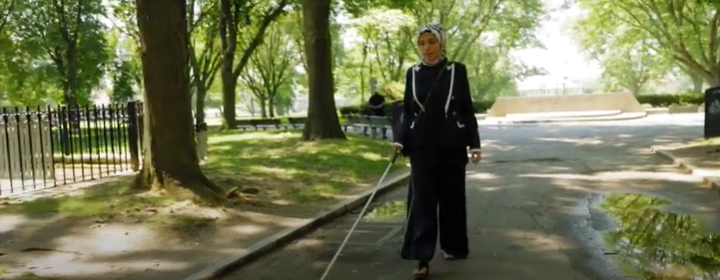 screengrab of Sara Minkara walking with a white cane through a city park