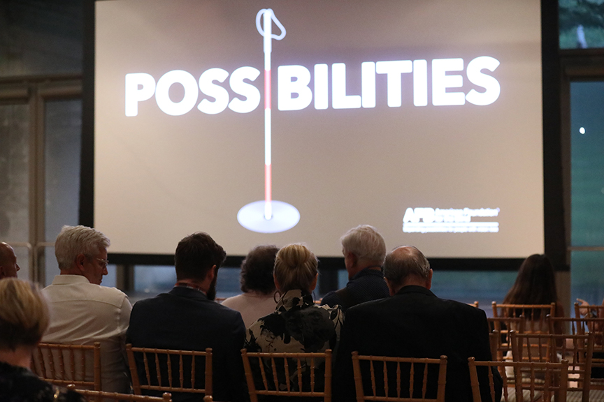 A group of movie screening attendees sit in front of a large projector screen with the Possibilities documentary logo.