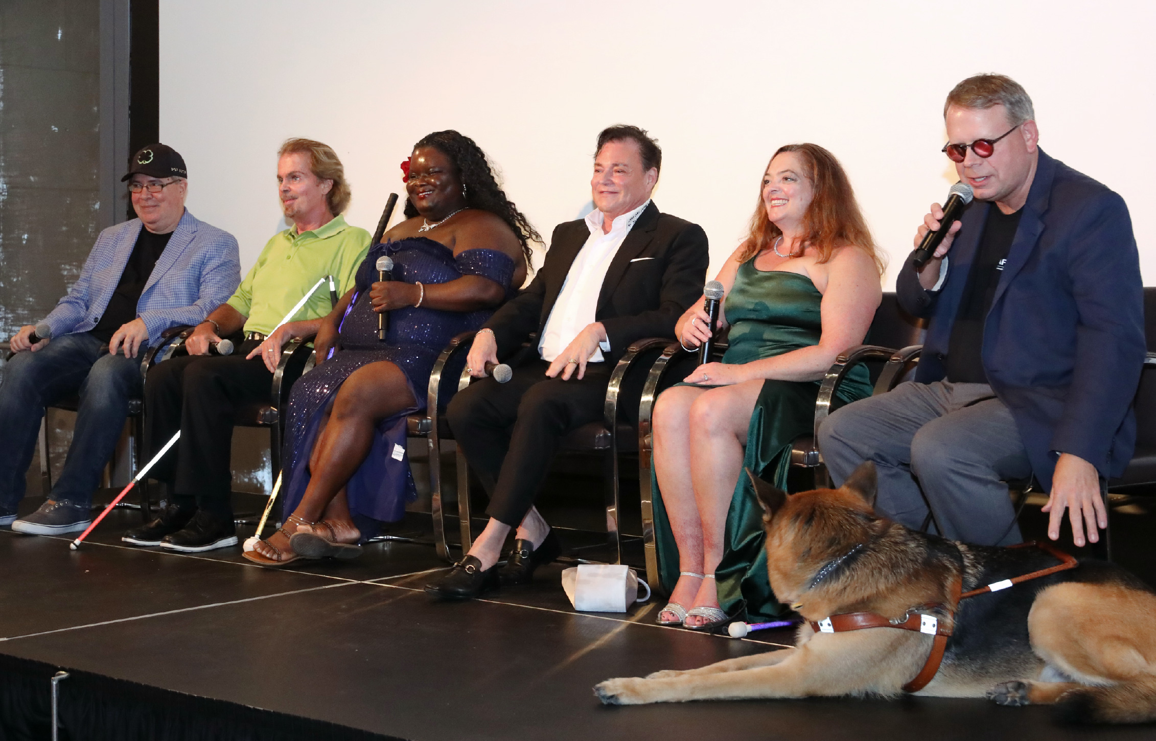 6 Panelists seated on stage, talking into mics and smiling towards the audience.