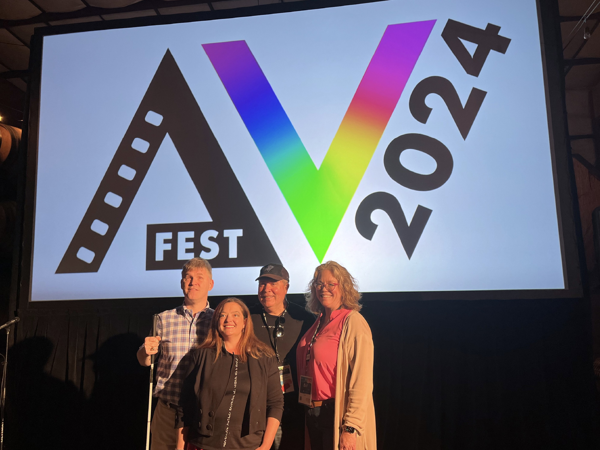 People smile in front of a screen with the AV Fest 2024 logo.