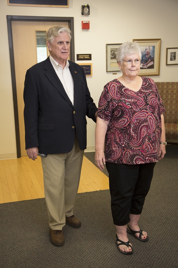 A person walking behind another individual as they hold on to their elbow.