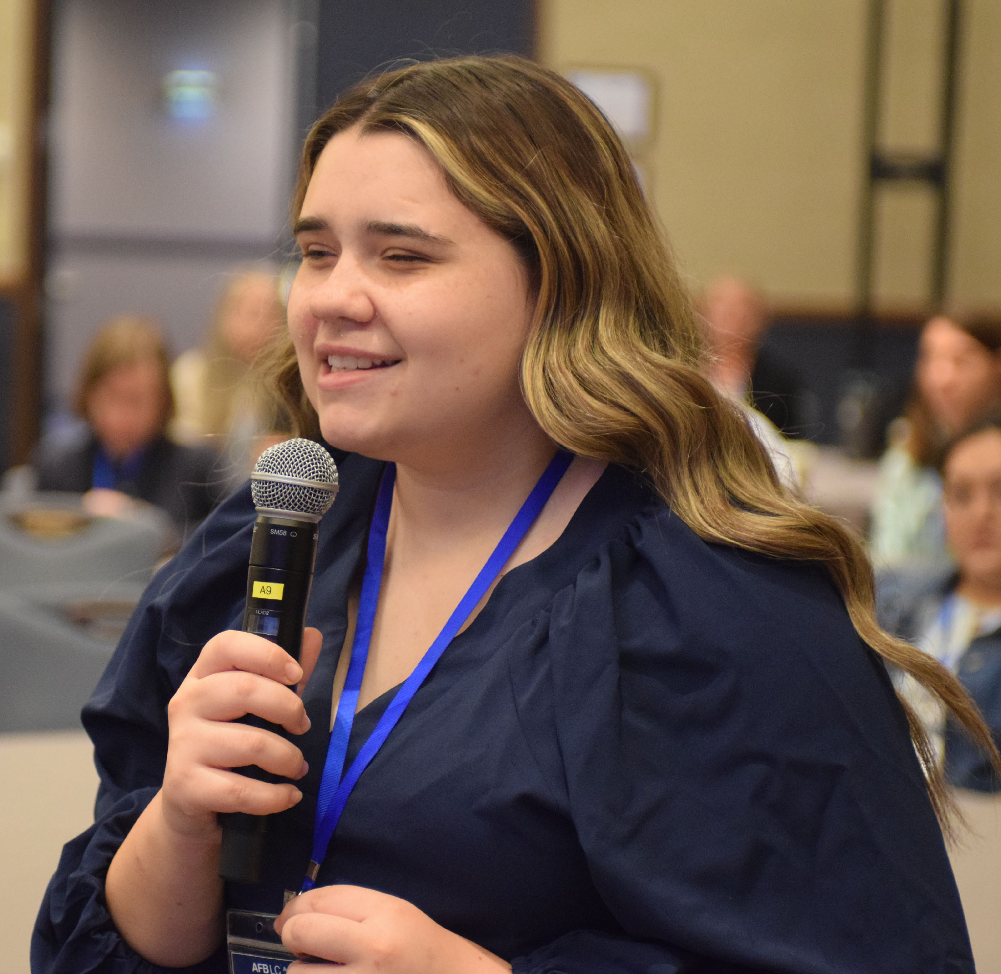 A young woman with low vision speaks in a crowd at an AFB event.